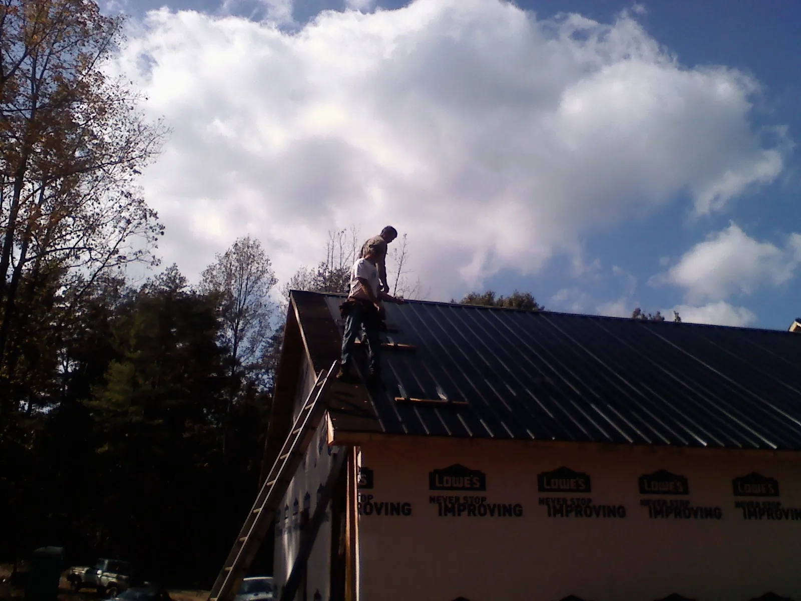 Roofer fastening dark metal panels high against a cloudy sky, from a Roof Inspection job in Burbank