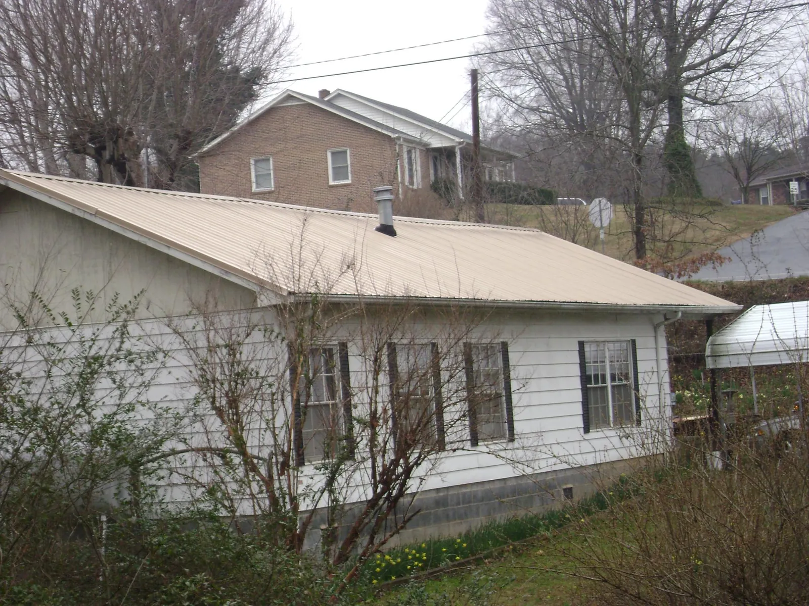 Tan metal roof on a white sided house set into a hillside — Commercial Roofing by Roofing Brothers in Burbank